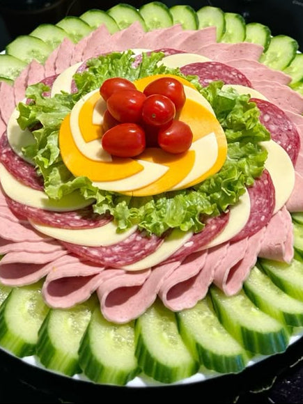 Decorative platter with sliced cucumbers, salami, and tomatoes on a black surface.
